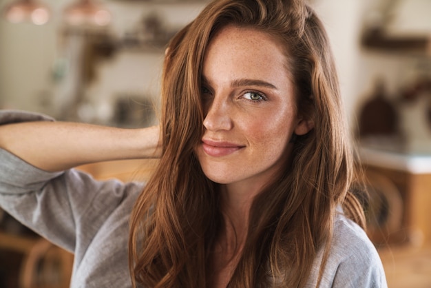 Picture of young cheerful beautiful optimistic happy pleased redhead woman indoors at home.