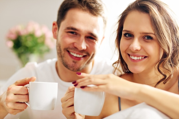 ベッドでコーヒーを飲む若いカップルの写真