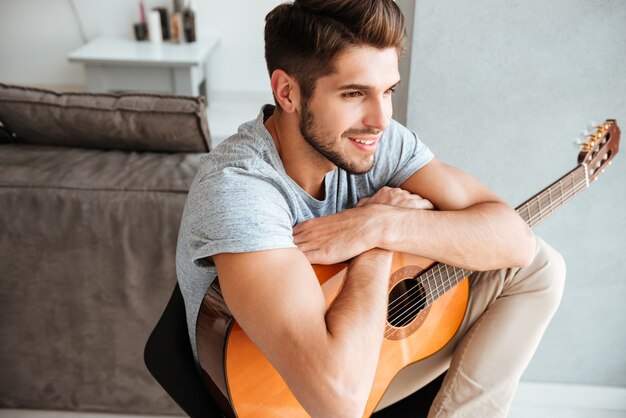 Foto di giovane uomo seduto con la chitarra su una sedia e guardare da parte.