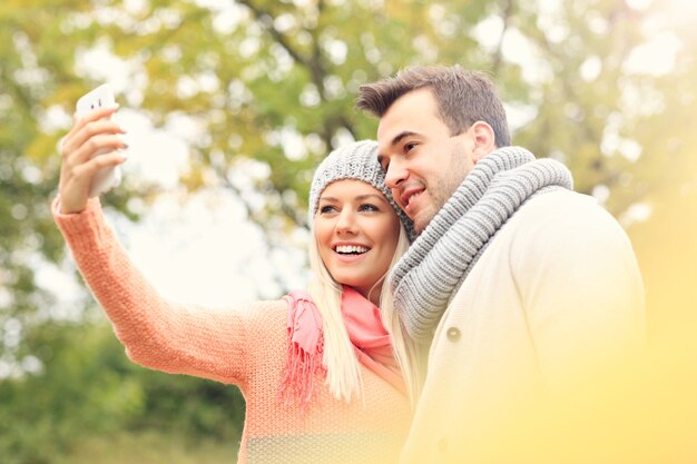 秋の公園でスマートフォンと若いロマンチックなカップルの写真