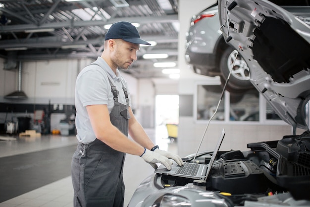 Picture of young worker type on keyboard. He looks at screen of laptop. Guy is doing diagnostics for car. He checkes its condition.