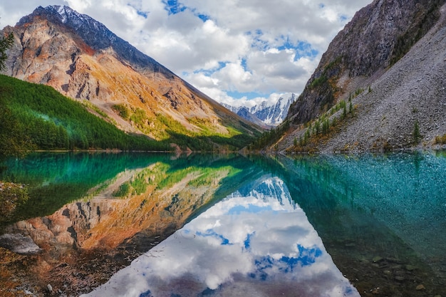 Picturesque mountain lake in the dramatic day, Altai. Beautiful reflection of mountains, sky and white clouds.