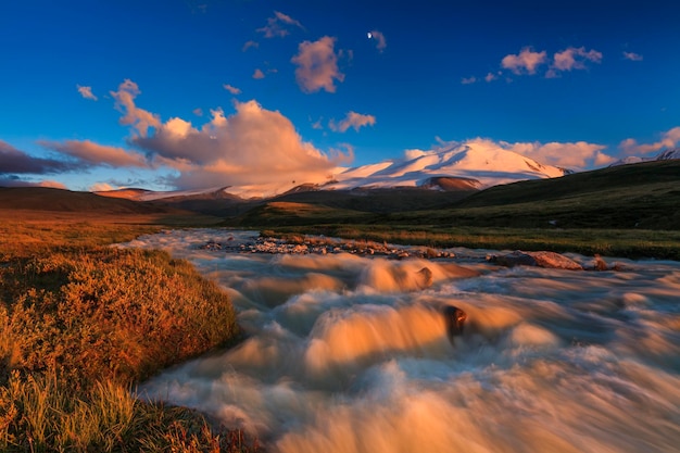 The picturesque mountain landscape with a creek at sunset sky background