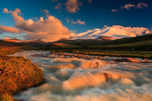 The picturesque mountain landscape with a creek at sunset sky background