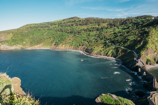 스페인의 화창한 날 바다의 바위 산 후안 데 가즈텔루가체(San Juan de Gaztelugatxe) 섬으로 이어지는 긴 통로의 그림 같은 전망