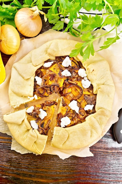 Pie of pumpkin, fried onions and soft cheese on parchment, napkin, parsley on a dark wooden board on top