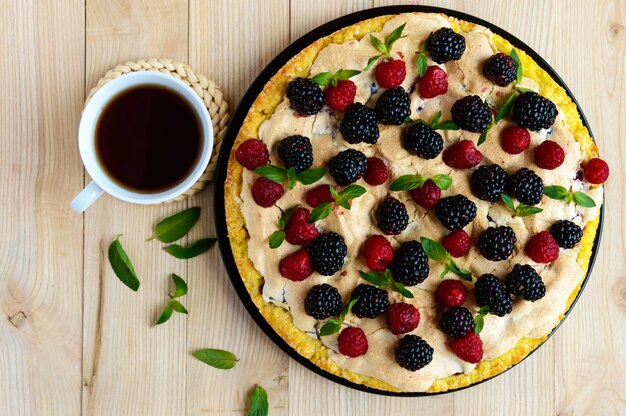 Torta con more e lamponi freschi, meringa all'aria, menta decorativa e tazza di tè