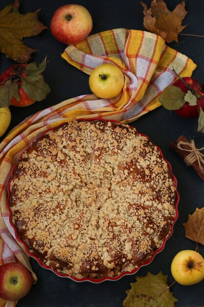 Pie with apples is located in a ceramic form on a dark background, top view, vertical orientation