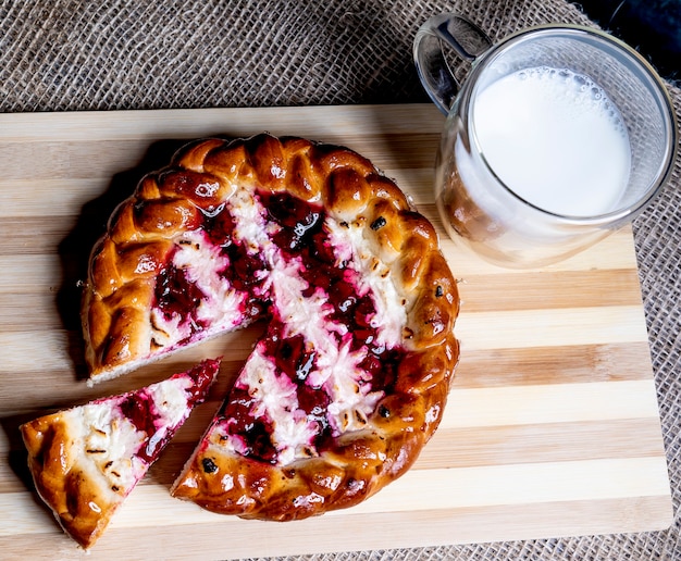 Pie with cherries and cottage cheese cut off a piece and a mug of milk.