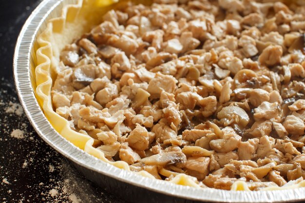 Pie with chicken in an aluminium form on a dark background close up