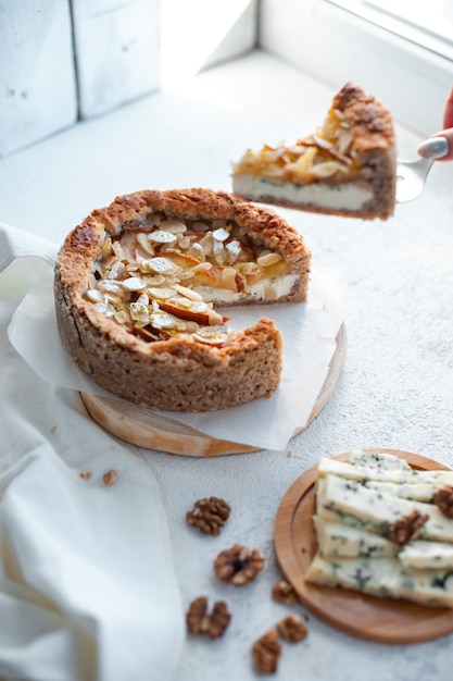 Torta con formaggio blu dor, pere e mandorle, tutto il giro su un piatto su un tavolo bianco.