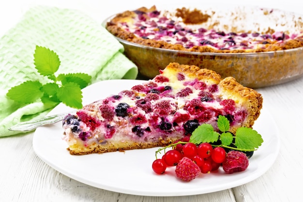 Pie with raspberries currants and cream sauce in a plate napkin and mint on light wooden board background