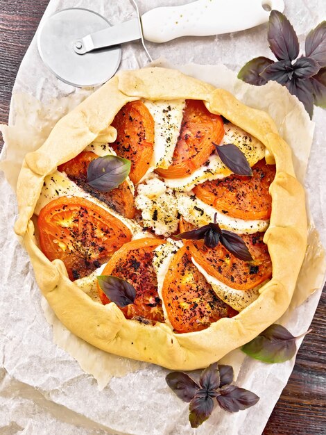 pie with tomatoes, curd cheese and purple basil on parchment on wooden board background 