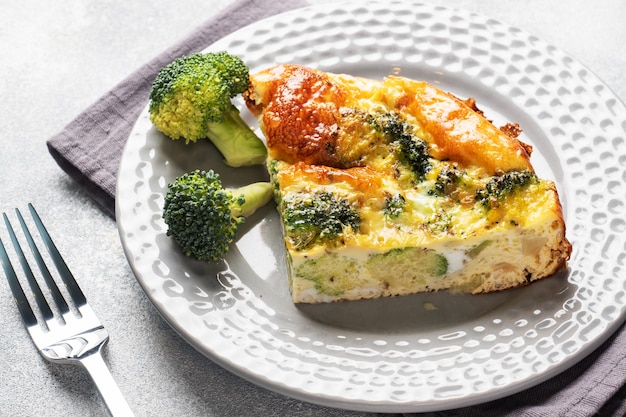 Piece Baked omelet with broccoli on a plate. Concrete table. Healthy diet food dish.