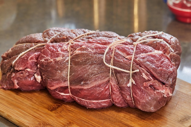 Piece of beef tied with special food ropes on wooden cutting board in home kitchen