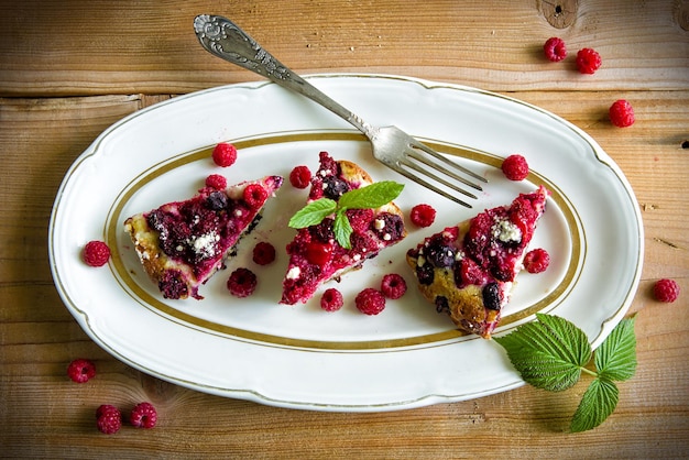 Кусок ягодного пирога малина красная смородина лист на тарелке на деревянной доске вид сверху