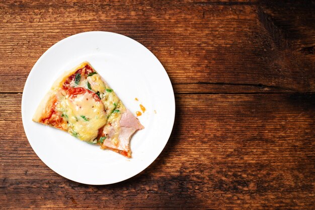 Piece of bitten piece of pizza on a plate on a wooden background