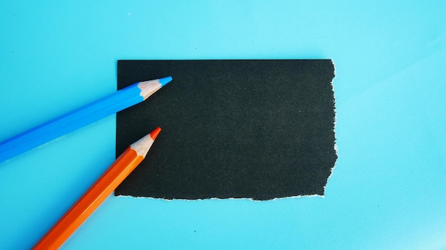 A piece of black paper with orange and blue pencils on it