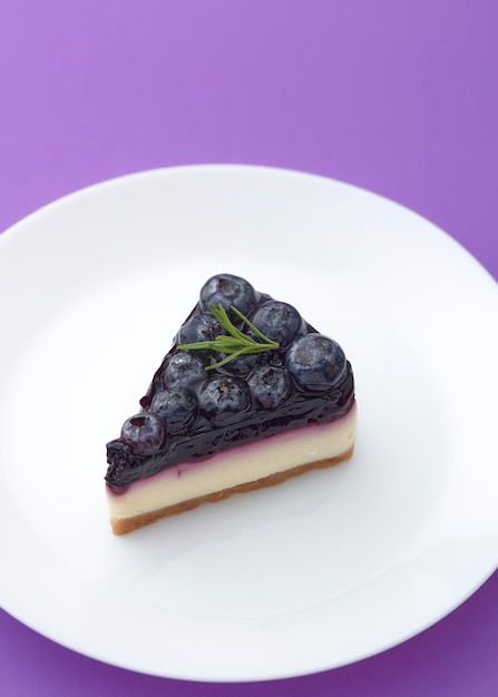 Piece of blueberry cheesecake on white plate on violet background