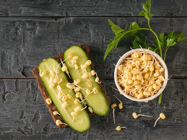 A piece of bread with cucumbers and sprouted mung beans on a dark wooden table. Dietary vegetarian food from sprouted grains.