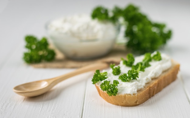 A piece of bread with curd cream and green parsley on white wooden table.