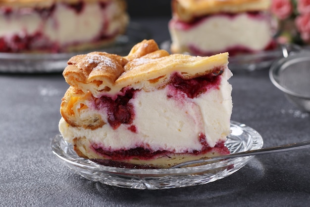 Piece of cake Karpatka with cherries close-up, traditional Polish cream pie on dark gray background.