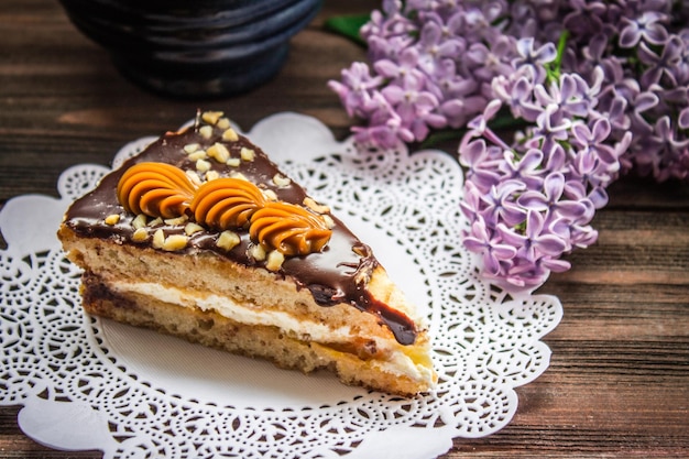 Piece of cake and a lilac on a brown wooden background