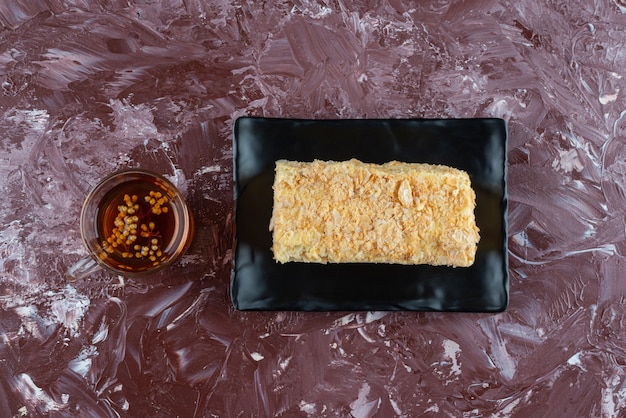 Piece of cake Napoleon on black tray with a glass of herbal tea .