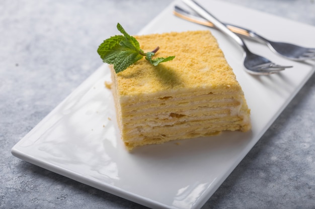 Piece of cake Napoleon on white plate on concrete              background, close up view. Traditional millefeuille dessert with puff pastry and custard, copy space.