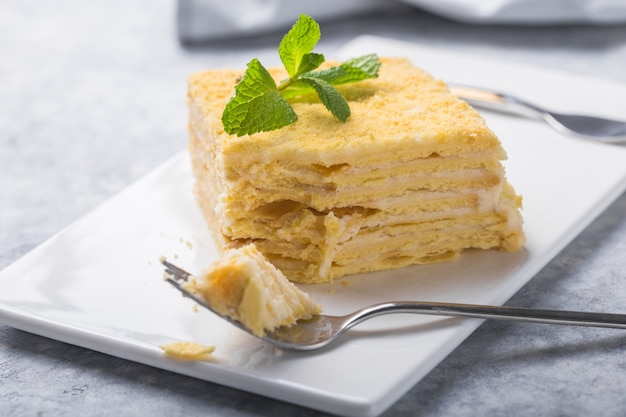 Piece of cake Napoleon on white plate on concrete              background, close up view. Traditional millefeuille dessert with puff pastry and custard, copy space.