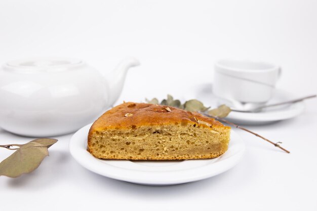 A piece of cake on a saucer with a cup for tea or coffee and a kettle