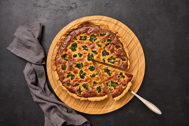 Piece of cake on spatula and quiche pie with broccoli tuna and cheese on round wooden cutting board