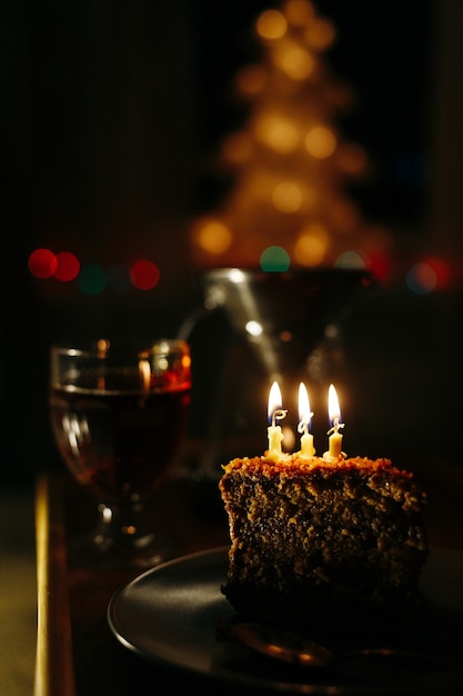 A piece of cake with burning candles in a dark room birthday or holiday greeting