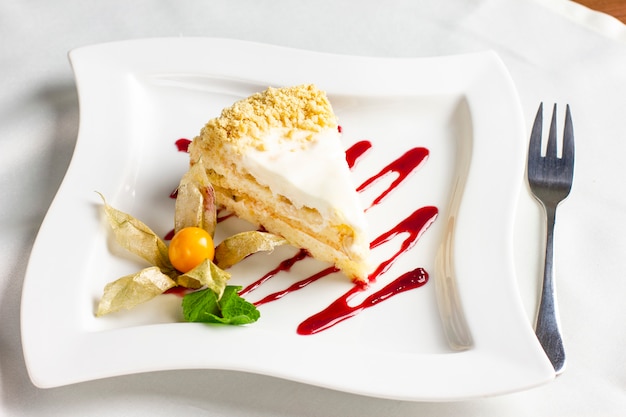 The piece of cake with cream and physalis on white plate