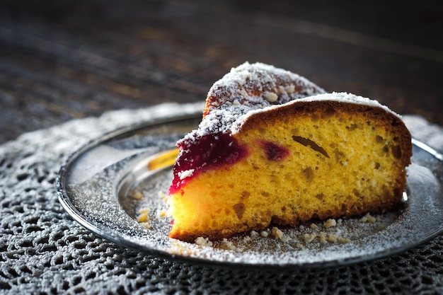 Piece of cake with icing sugar and jam on the lace napkin close up