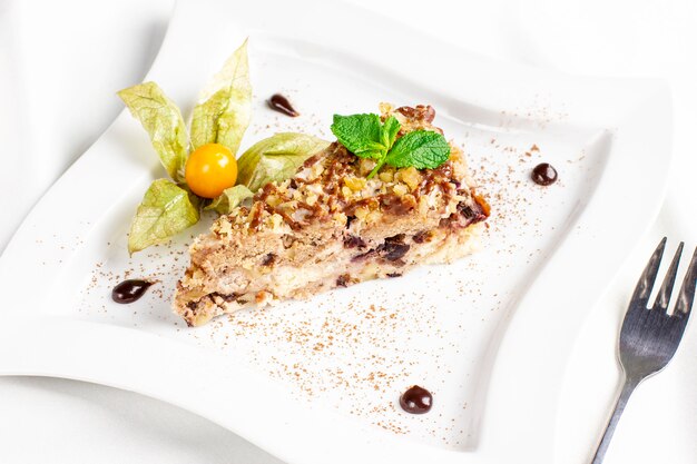 The piece of cake with nuts, dried fruits and physalis on white plate