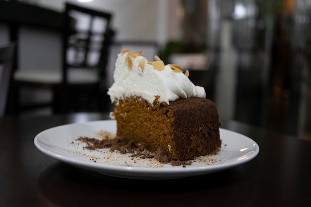 A piece of carrot cake covered with cream Selective focus In the background the cafeteria