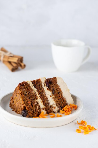 A piece of carrot cake with coconut cream and a cup of tea on a light background