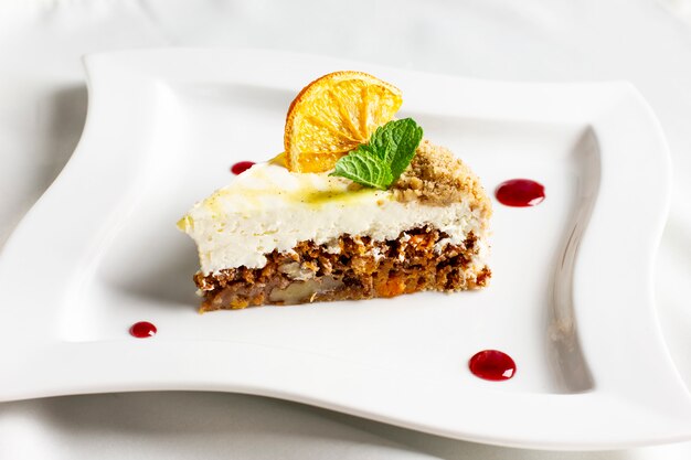 The piece of carrot cake with cream, nuts and dried orange on white plate