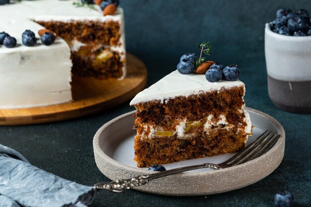 Piece of carrot cake with walnuts and blueberry on dark wood background. Local food. Traditional american cake. Cake for thanksgiving day. Autumn cake.