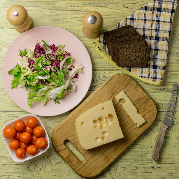 A piece of cheese and fresh vegetables next to a wooden surface Preparation of a vegetarian salad