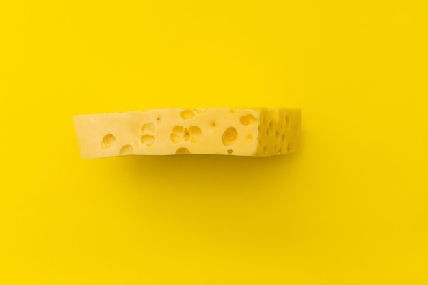 Кусок сыра с дырками лежит на желтом фоне монохромных продуктов