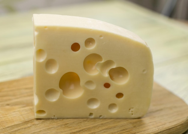 A piece of cheese with large holes on a wooden cutting board