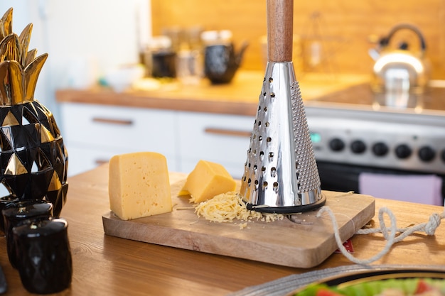 A piece of cheese on a wooden board next to an iron grater