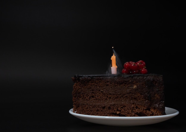 Piece of chocolate birthday cake with one extinguished candle
on white plate on deep black backgroun