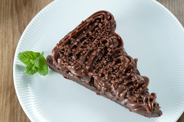 Pezzo di fetta di brownie al cioccolato con fragole e glassa di cioccolato tavolo in legno con menta e gocce di cioccolato sullo sfondo vista dall'alto