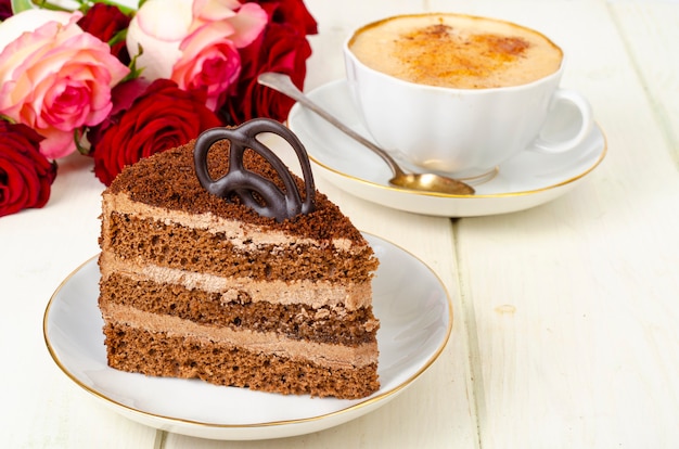 Piece of chocolate cake, cappuccino, flowers on table.