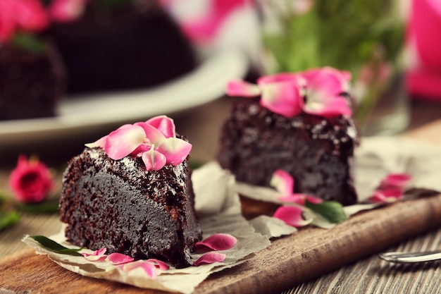 Piece of chocolate cake decorated with flowers on brown wooden table