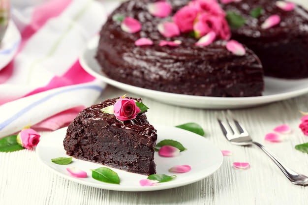 Piece of chocolate cake decorated with flowers on white wooden table