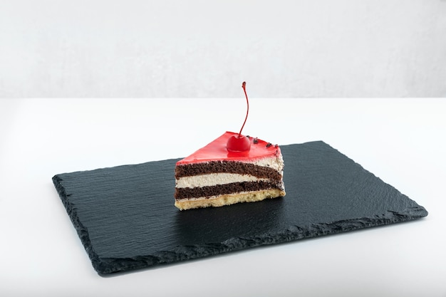 Piece of chocolate cake with maraschino cherry. Side view to piece of cake on black plate.